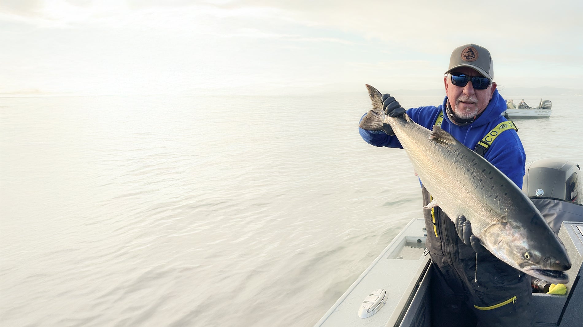 Astoria Fishing Guide Don Peck is Holding a Big Salmon Standing in a boat on a large river.